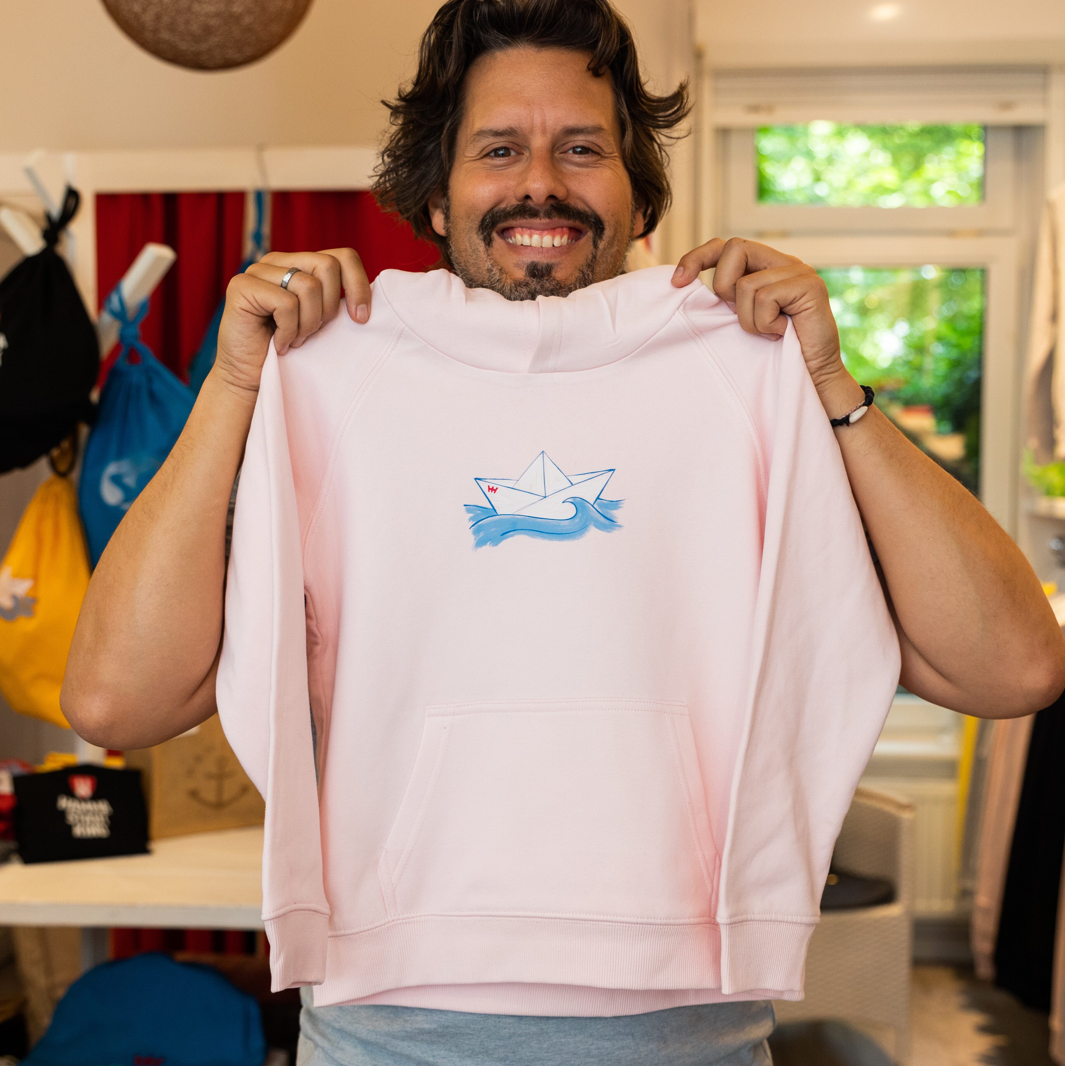 Daniel hält grinsend einen rosafarbenen Kinder-Hoodie in die Kamera