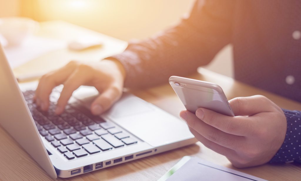 Person arbeitet mit Laptop und Smartphone
