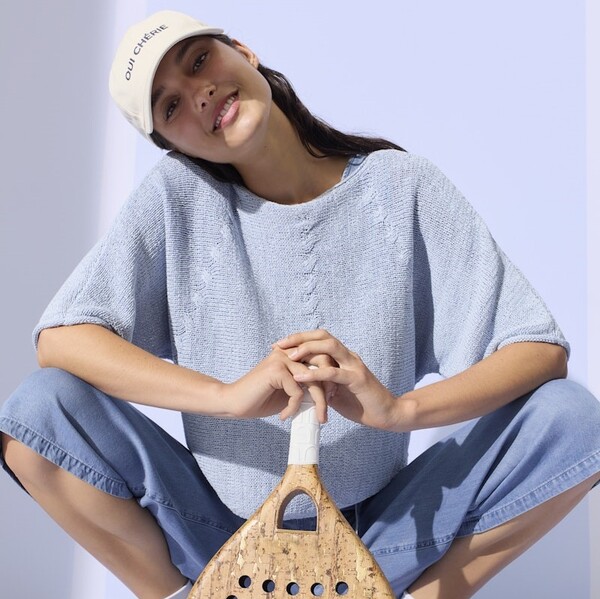 Model in einem babyblauen Strick T-Shirt und einer weißen Baseballcap