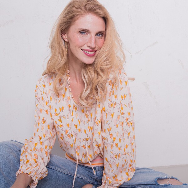 Emily van den Bergh F/S 2026 - weiße Bluse mit orangenen Muster und einer Jeanshose